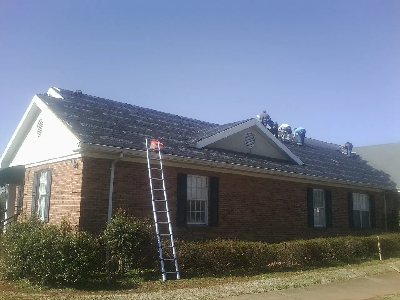 Crew tearing shingles off a brick ranch roof with a ladder set — Metal Roof Repair work by our crew in Hartford